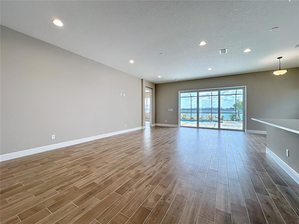 An open-concept living area features wood-look tile flooring, recessed lighting, and sliding glass doors — 247 MONET TRAIL, BRADENTON, FL