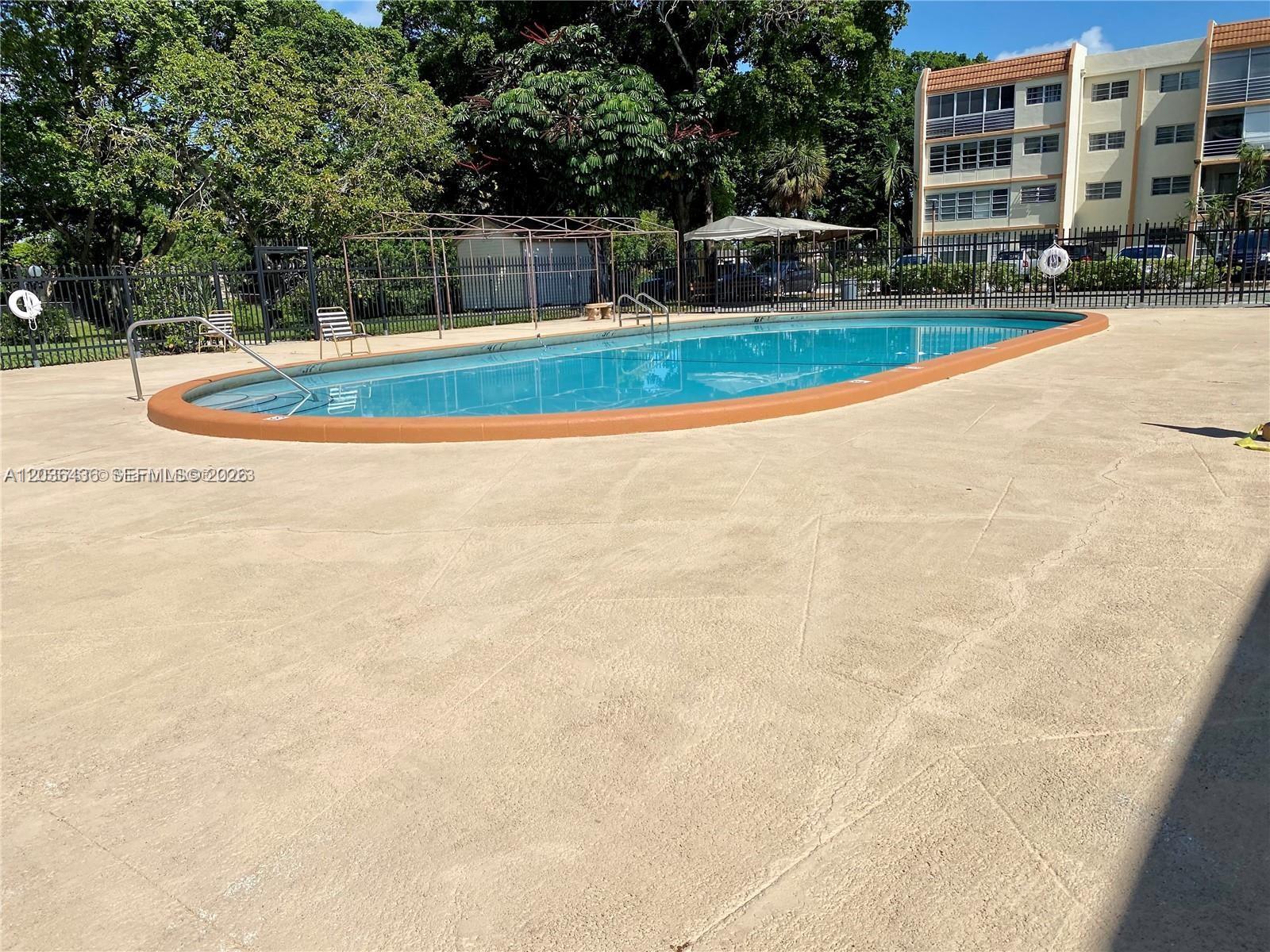An outdoor swimming pool with a brown coping sits on a concrete deck — 2301 NW 41st Ave # 302, Lauderhill FL 33313, LAUDERHILL, FL
