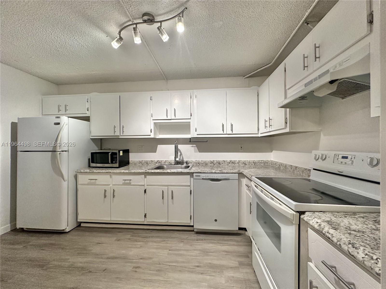 A kitchen features white cabinets, white appliances, speckled countertops, and wood-look flooring — 1470 NE 125th Ter # 210, North Miami FL 33161, NORTH MIAMI, FL