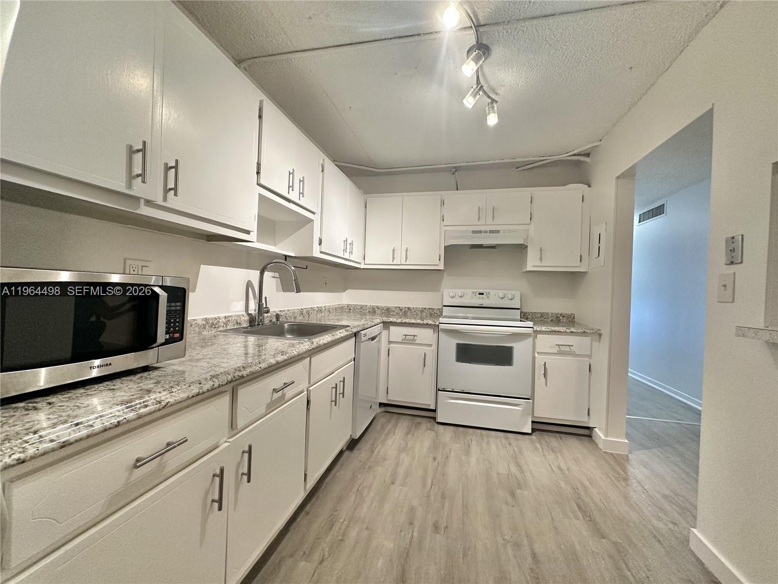 A kitchen features white cabinets, granite countertops, stainless steel appliances, and light wood-look flooring — 1470 NE 125th Ter # 210, North Miami FL 33161, NORTH MIAMI, FL