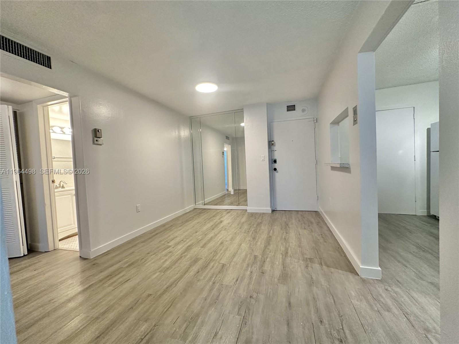 This room features light wood-look flooring, white walls, a mirrored closet, and a white door — 1470 NE 125th Ter # 210, North Miami FL 33161, NORTH MIAMI, FL