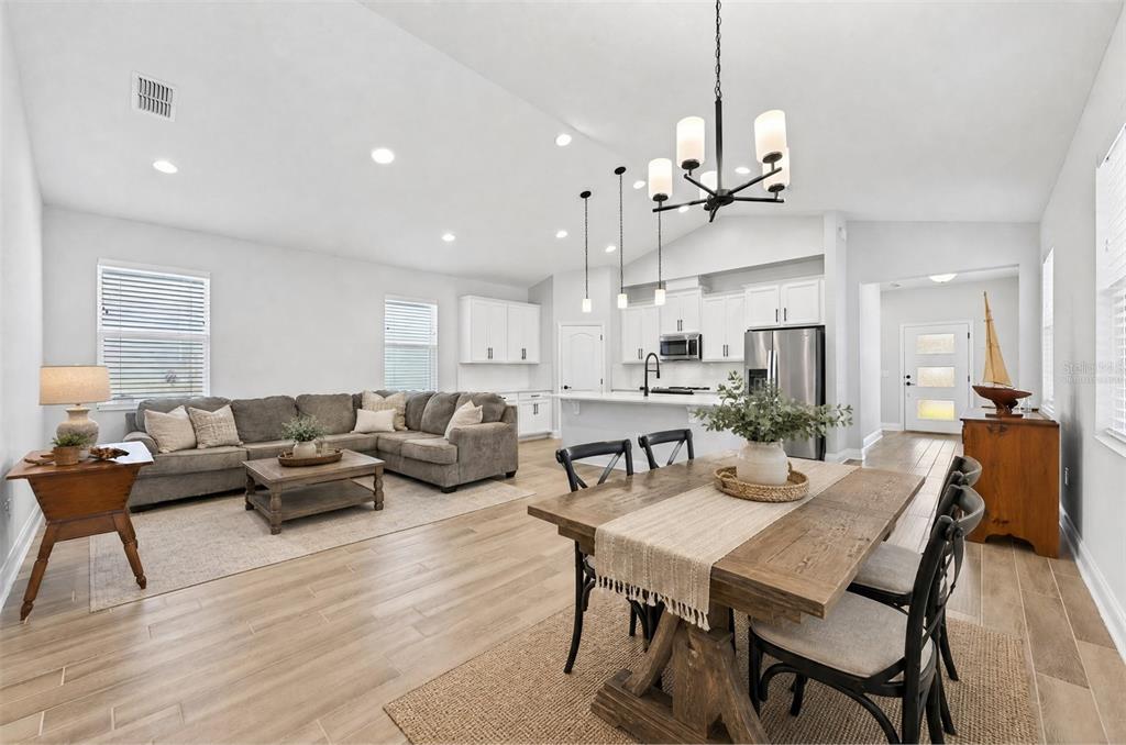 An open-concept living and dining area features light wood floors, white cabinetry, and neutral furniture — 606 DOGFISH LANE, DEBARY, FL