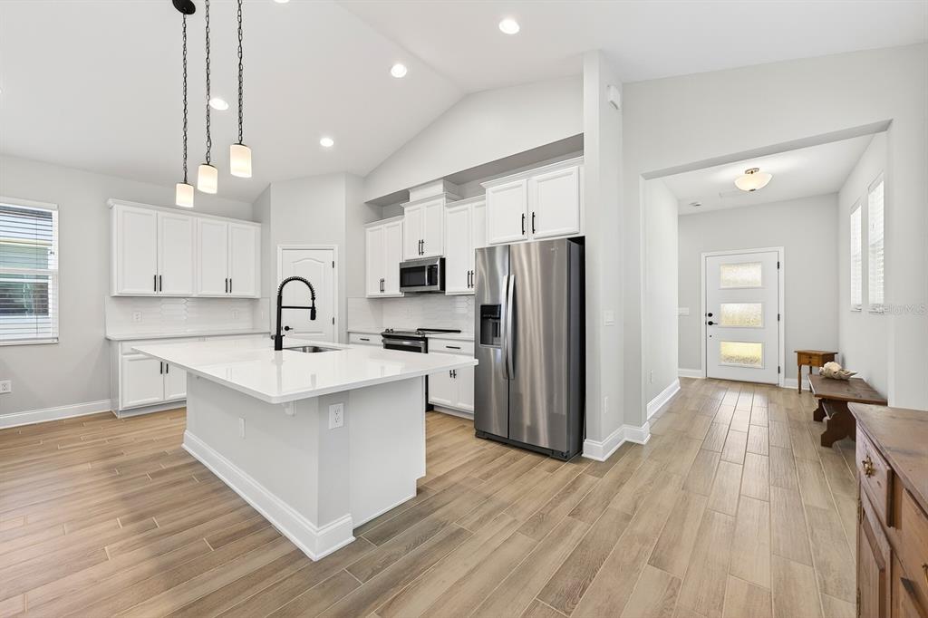 A modern kitchen features white cabinetry, a large island with a sink, and stainless appliances — 606 DOGFISH LANE, DEBARY, FL