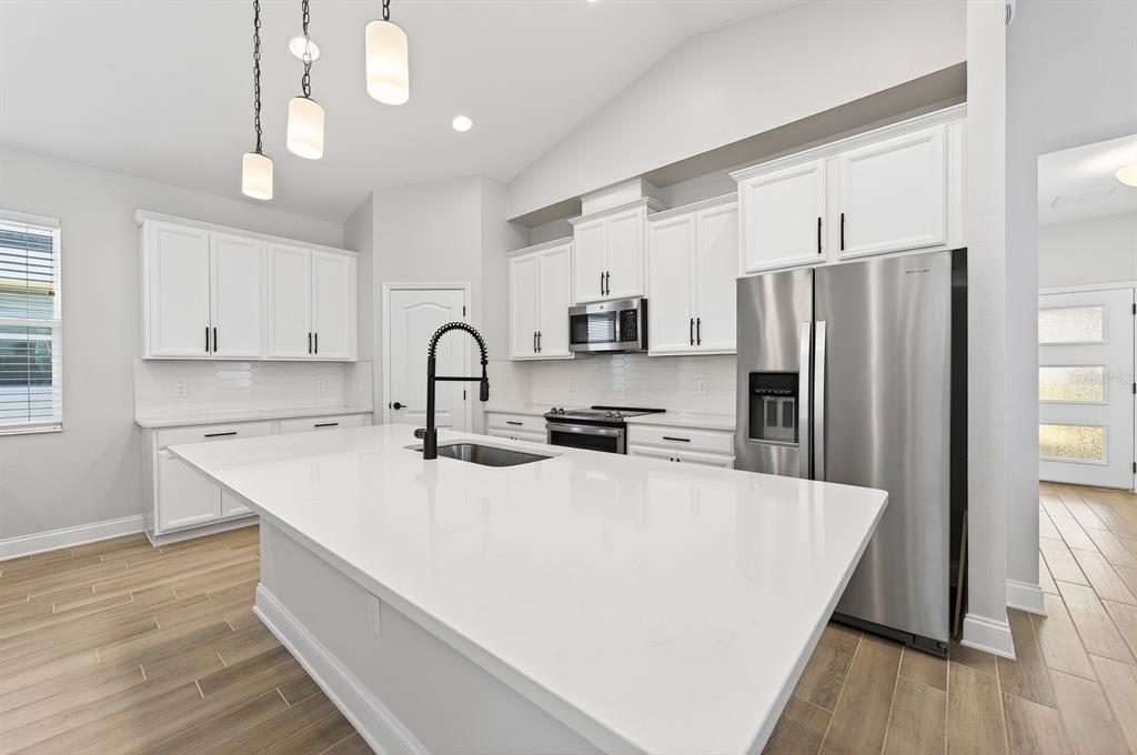 A modern kitchen features white cabinetry, a large quartz island, and stainless steel appliances — 606 DOGFISH LANE, DEBARY, FL