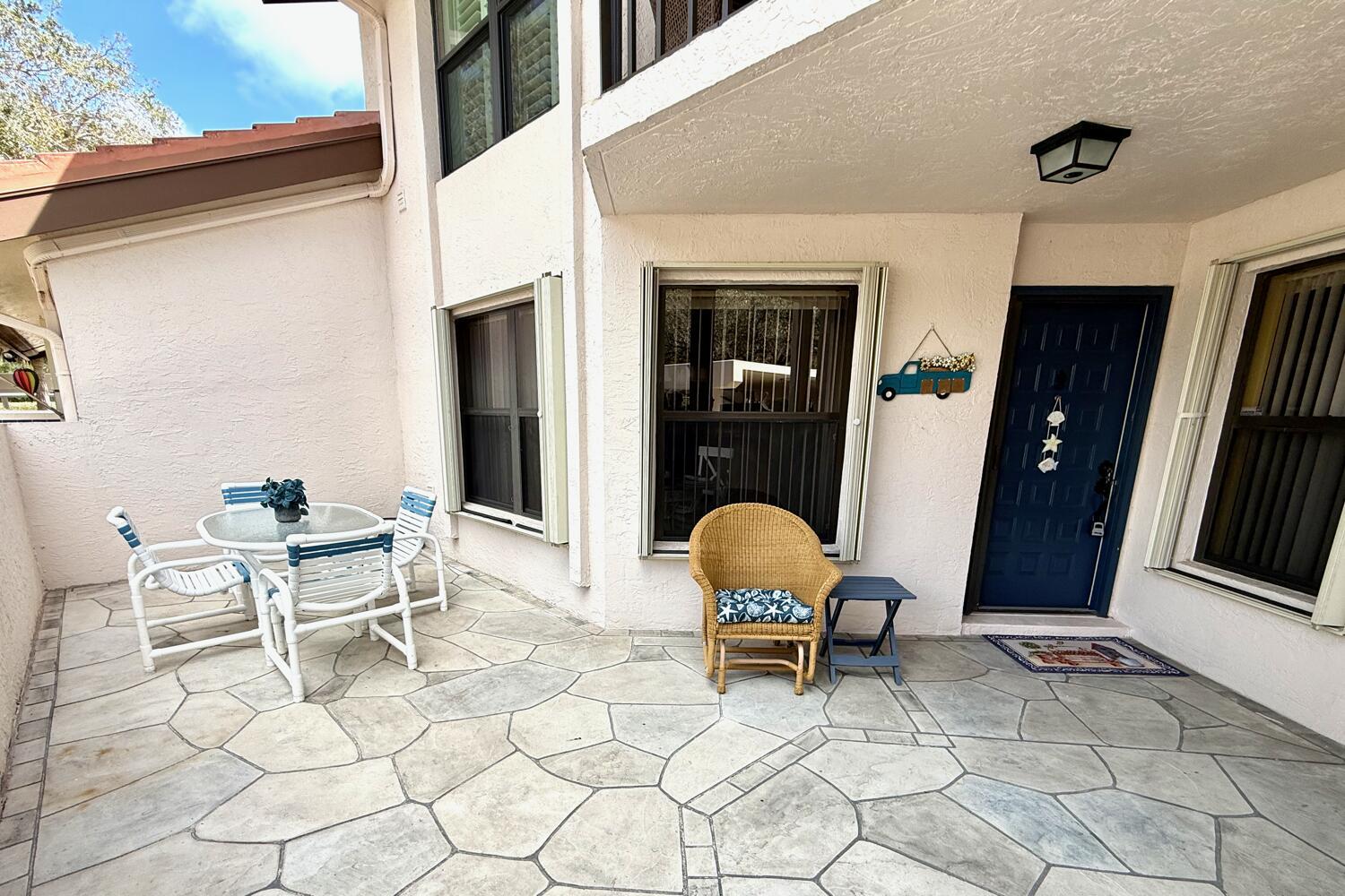 A patio features stone flooring, a dining set, a wicker chair, and a blue door — 6030 SE Martinique Drive # 102, Stuart FL 34997, STUART, FL