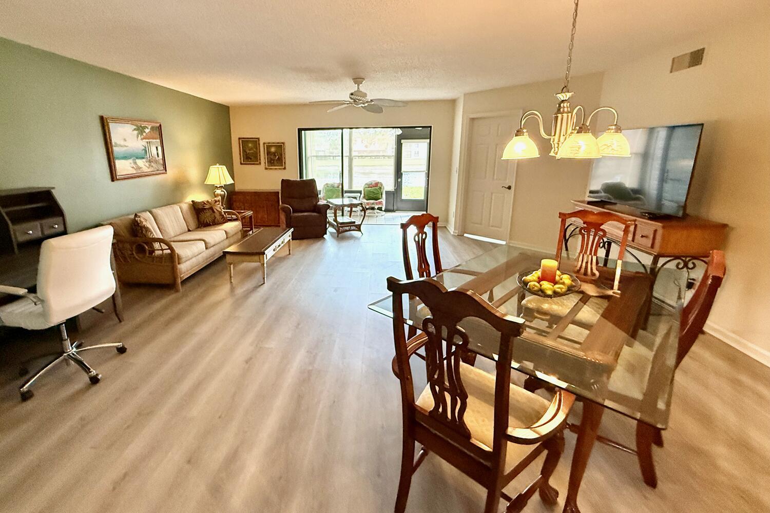 An open-concept living and dining area features light wood-look flooring and a glass-topped dining table — 6030 SE Martinique Drive # 102, Stuart FL 34997, STUART, FL