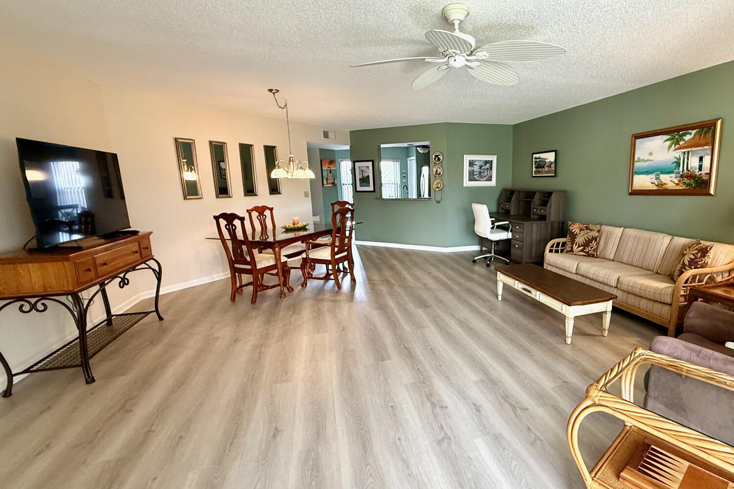 An open-concept living and dining area features light wood-look flooring and a sage green wall — 6030 SE Martinique Drive # 102, Stuart FL 34997, STUART, FL