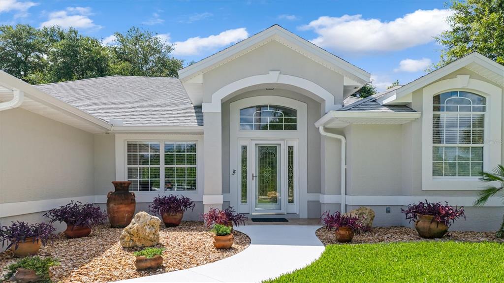 The exterior of a single-story house features a light-colored facade, arched entryway, and gravel landscaping — 48 BARRING PLACE, PALM COAST, FL