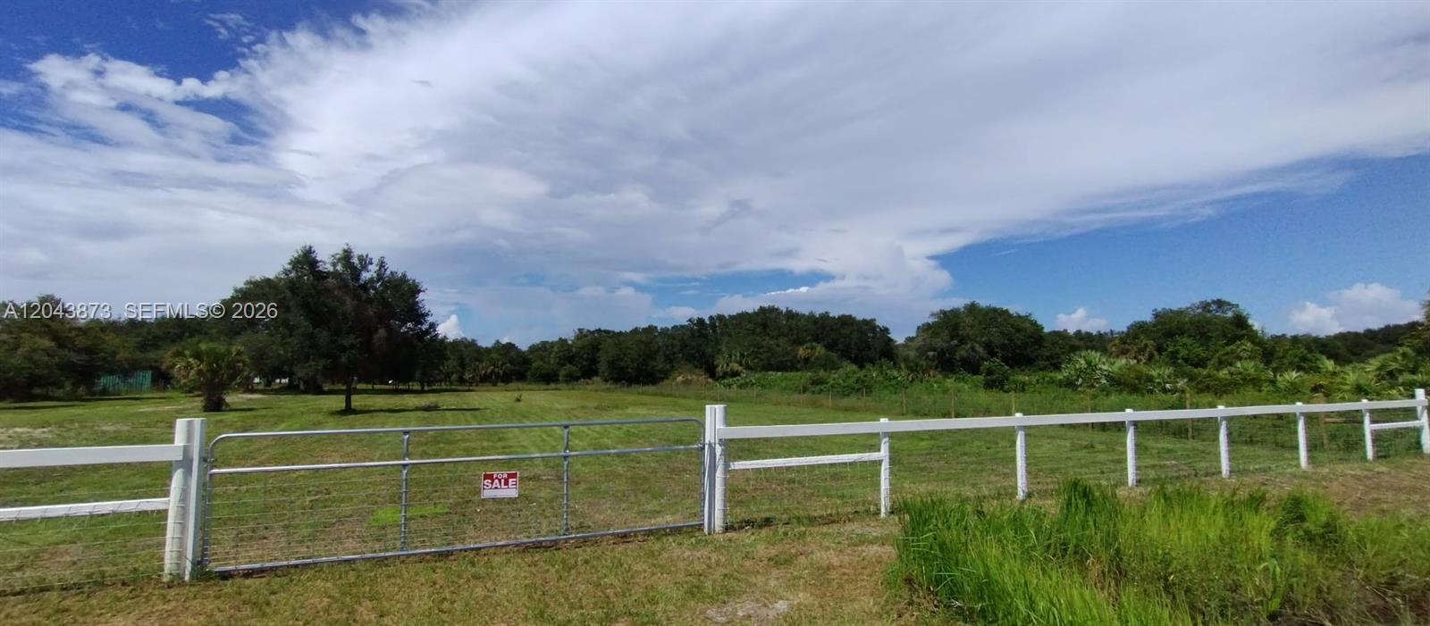 A gated entrance with a white fence opens onto a grassy, tree-lined vacant lot — 18611 NW 304 st, Okeechobee FL 34972, OKEECHOBEE, FL