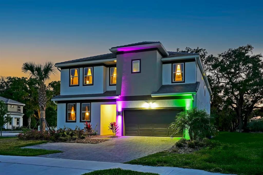 A two-story suburban house features exterior accent lighting in purple and green at dusk — 4441 GANESHA LOOP, KISSIMMEE, FL