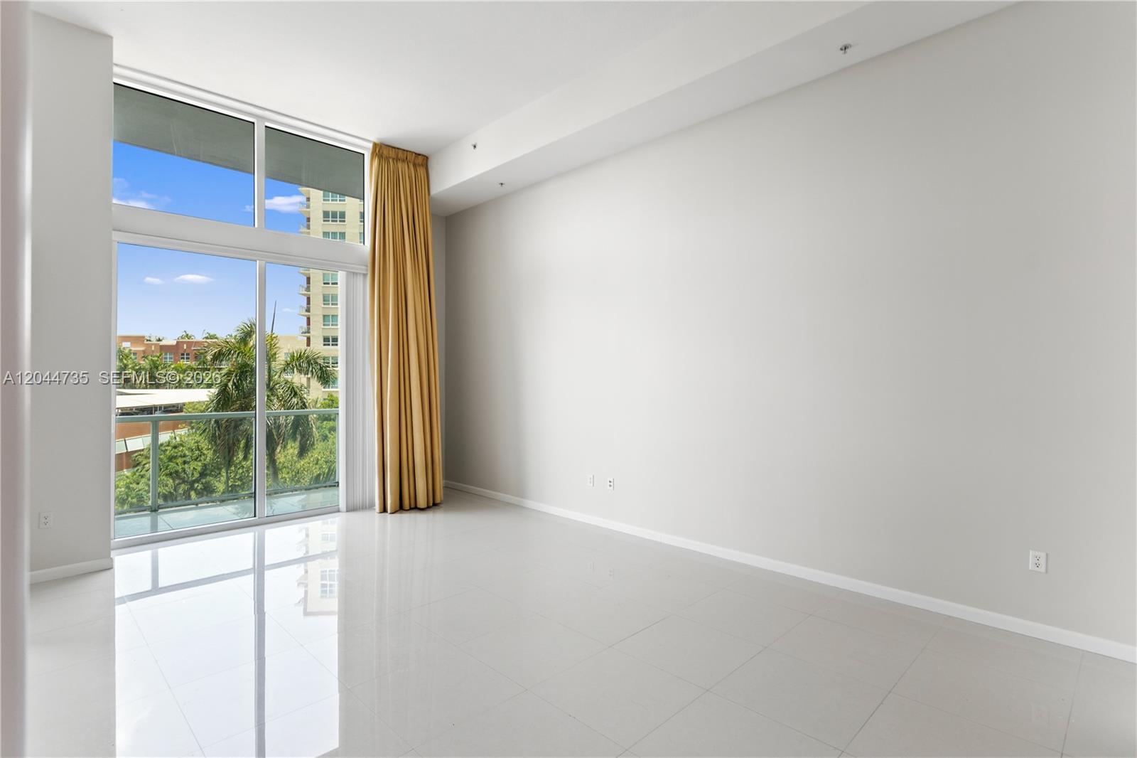 An empty room features white tile flooring, a large window with gold curtains, and a balcony — 1900 N Bayshore Drive Dr # 715, Miami FL 33132, MIAMI, FL