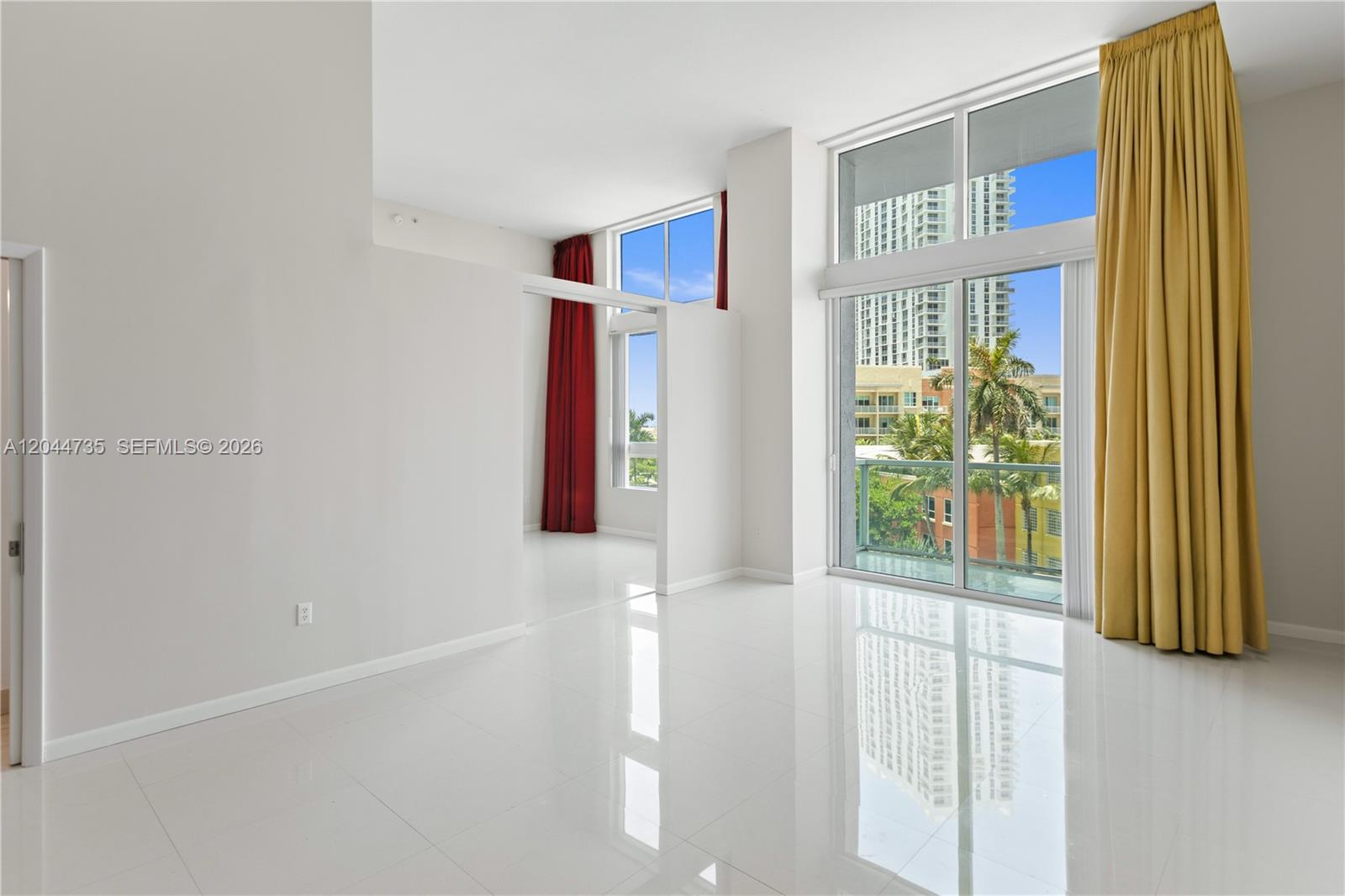 A bright, empty room features white tile floors, floor-to-ceiling windows, and red and gold curtains — 1900 N Bayshore Drive Dr # 715, Miami FL 33132, MIAMI, FL