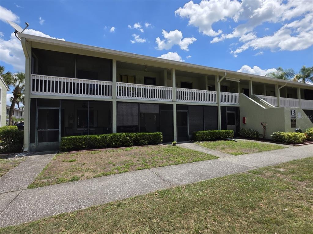 A two-story apartment building features screened balconies, white railings, and a concrete walkway — 20857 HAULOVER COVE UNIT B14, LUTZ, FL