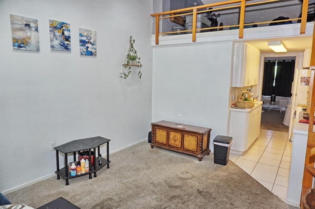 A living room with carpeted flooring, a wooden chest, and a loft area above — 20857 HAULOVER COVE UNIT B14, LUTZ, FL