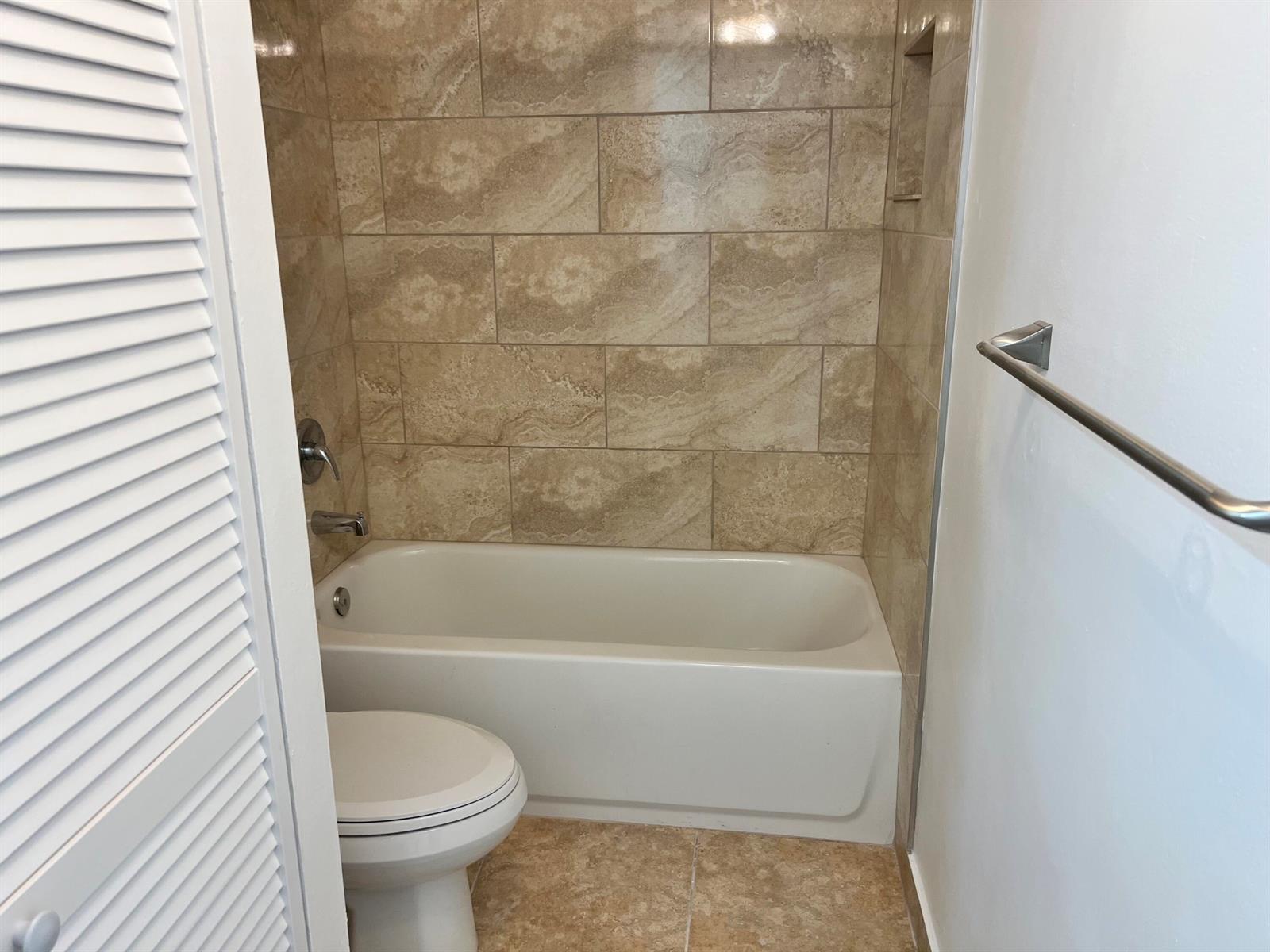 A bathroom features a white bathtub with tan tiled walls and a nearby toilet — 3114 31st Way, West Palm Beach FL 33407, WEST PALM BEACH, FL