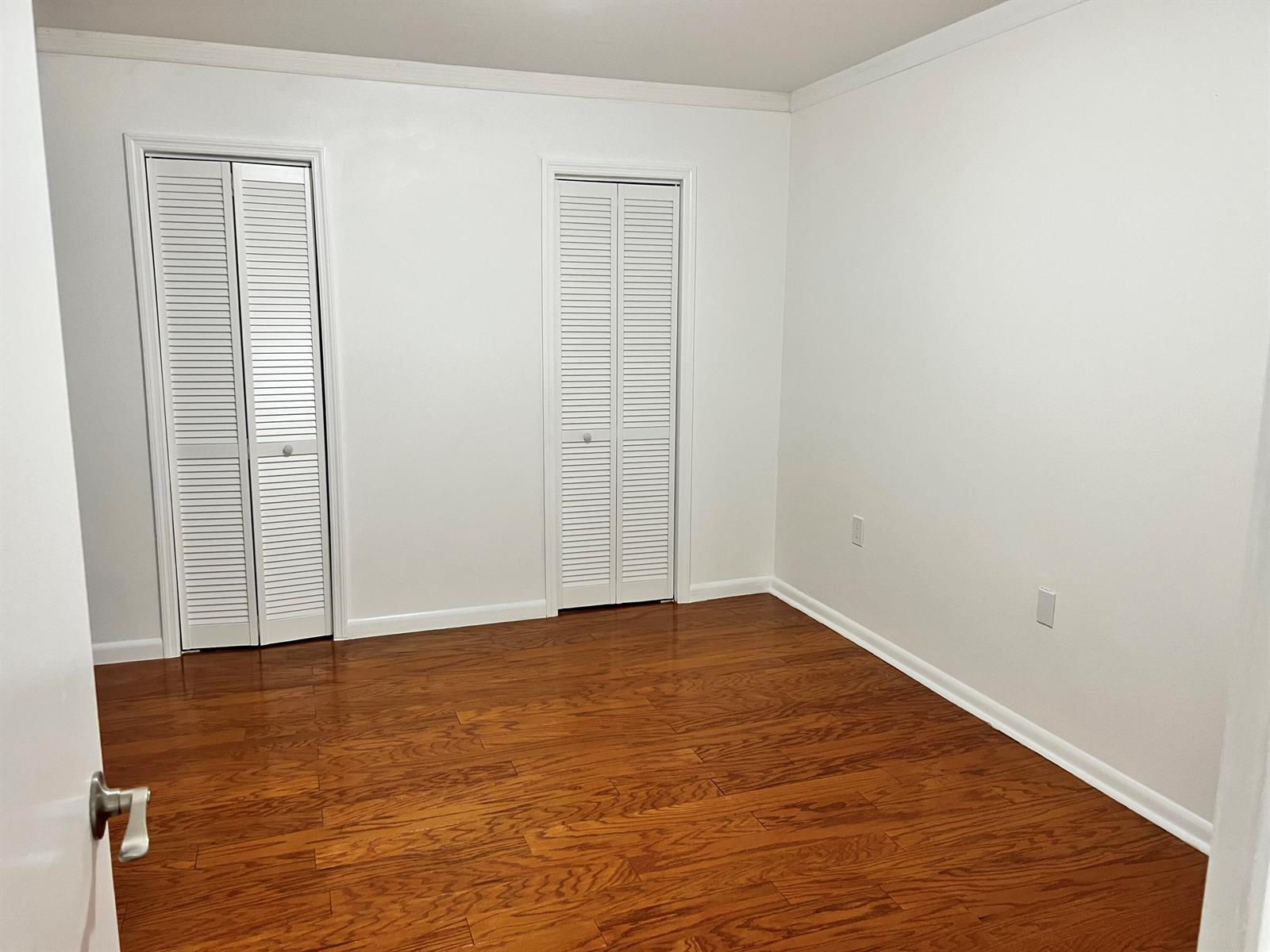 An empty bedroom features white walls, two louvered closet doors, and hardwood flooring — 3114 31st Way, West Palm Beach FL 33407, WEST PALM BEACH, FL
