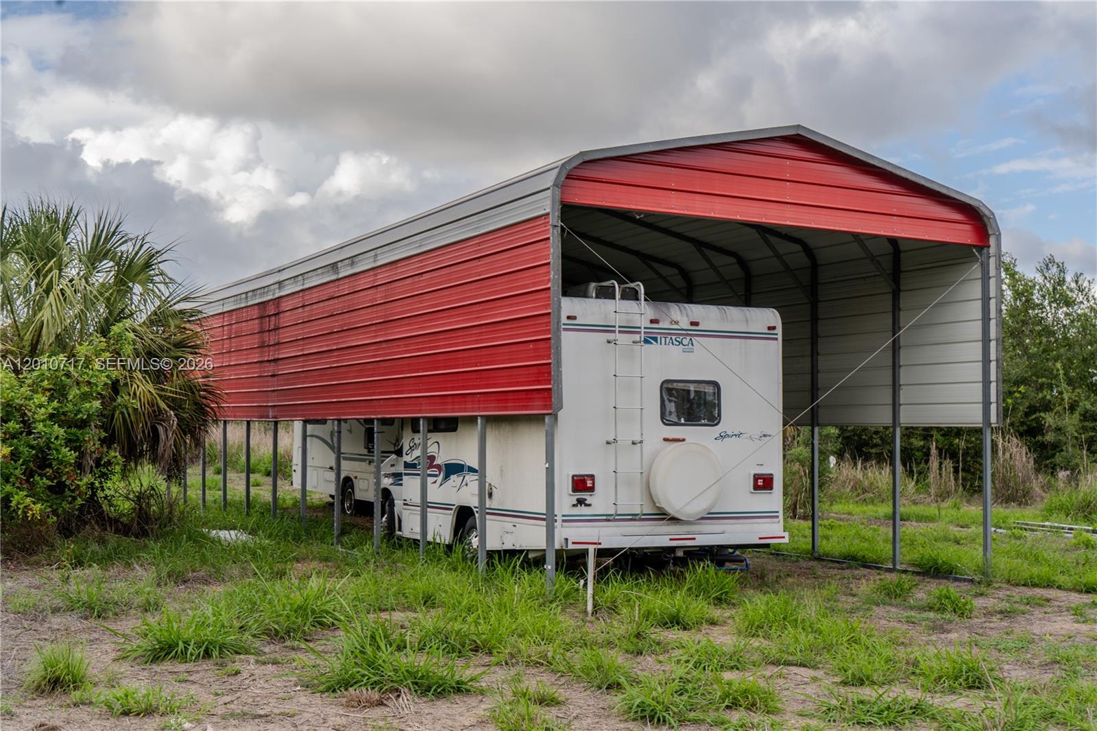 An Itasca Spirit motorhome is parked under a red and grey metal carport structure — 3921 Ft. Denaud Rd, La Belle FL 33935, LA BELLE, FL