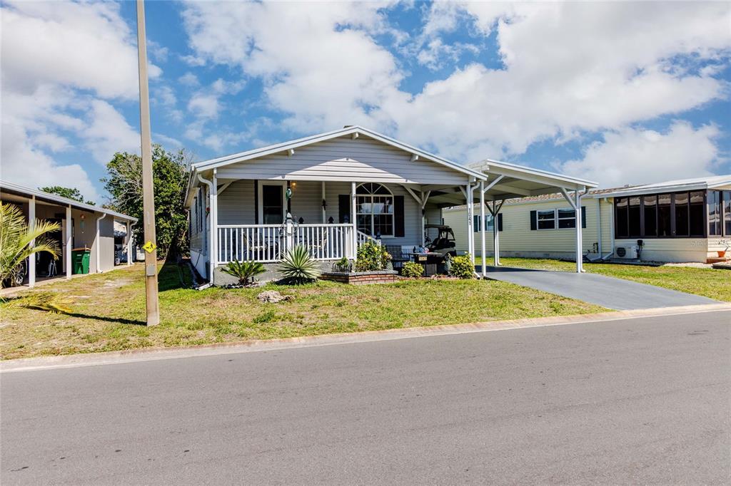 A light gray manufactured home with a front porch and attached carport sits on grass — 2100 KINGS HIGHWAY #1041, PUNTA GORDA, FL