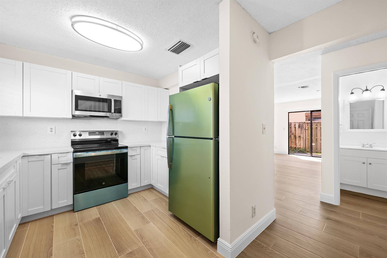 A kitchen with white cabinets, stainless steel appliances, and a green refrigerator next to a bathroom — 3281 E Golf Boulevard # 12, Pompano Beach FL 33064, POMPANO BEACH, FL