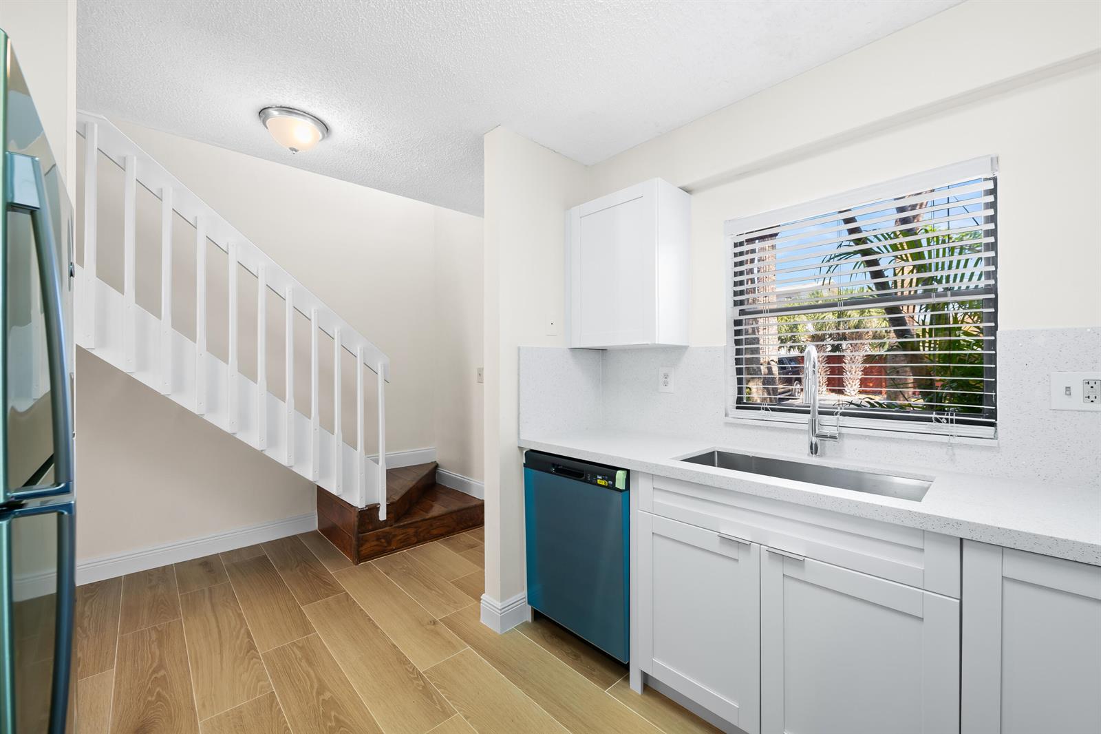 A kitchen with white cabinets, quartz countertops, a stainless steel sink, and a wooden staircase — 3281 E Golf Boulevard # 12, Pompano Beach FL 33064, POMPANO BEACH, FL