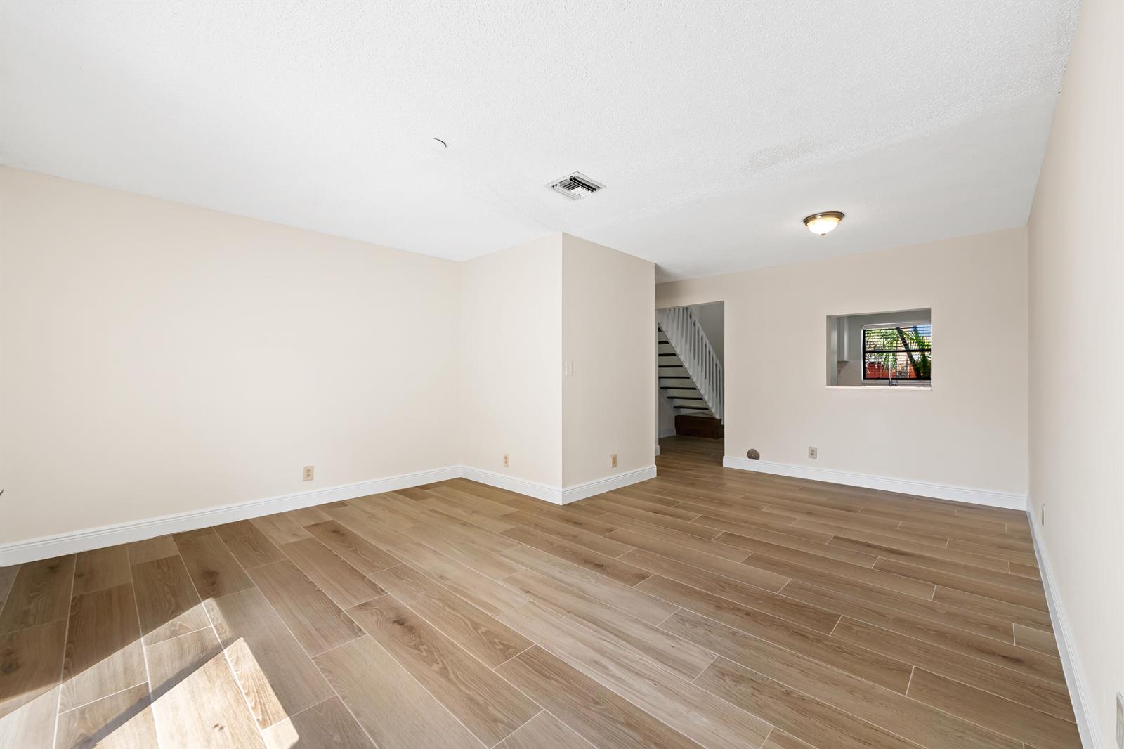 An empty room with light wood-look tile flooring, beige walls, and a view of stairs — 3281 E Golf Boulevard # 12, Pompano Beach FL 33064, POMPANO BEACH, FL