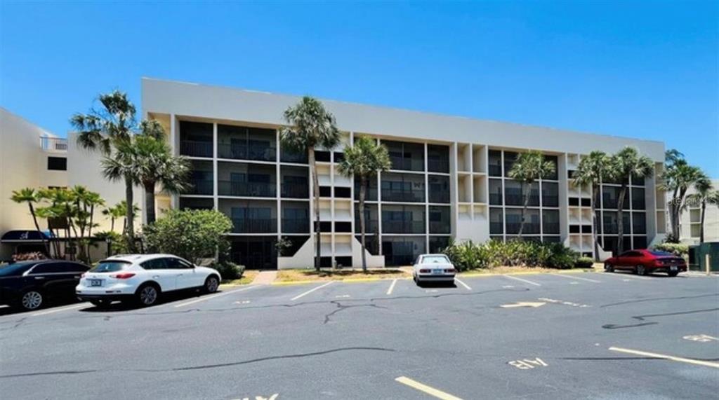 A multi-story apartment building with a parking lot in the foreground under a clear sky — 6120 43RD STREET W UNIT 102B, BRADENTON, FL
