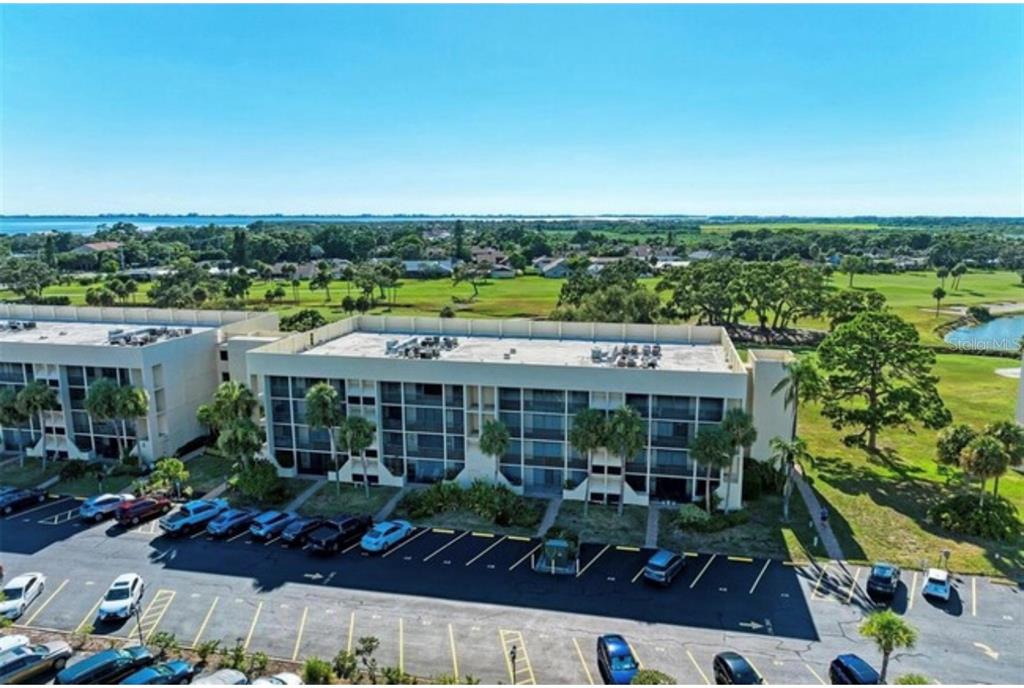 An aerial view shows a multi-story apartment building with a parking lot and golf course — 6120 43RD STREET W UNIT 102B, BRADENTON, FL