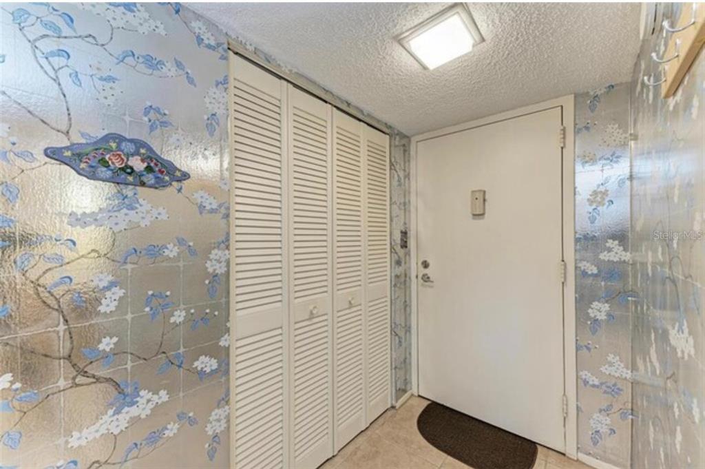 An entryway features floral wallpaper, a white louvered closet, and a white front door — 6120 43RD STREET W UNIT 102B, BRADENTON, FL