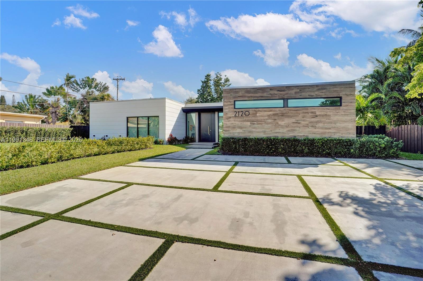 A modern single-story house features a wood-paneled facade, a concrete driveway, and a landscaped yard — 2120 NE 197th Ter, Miami FL 33179, MIAMI, FL