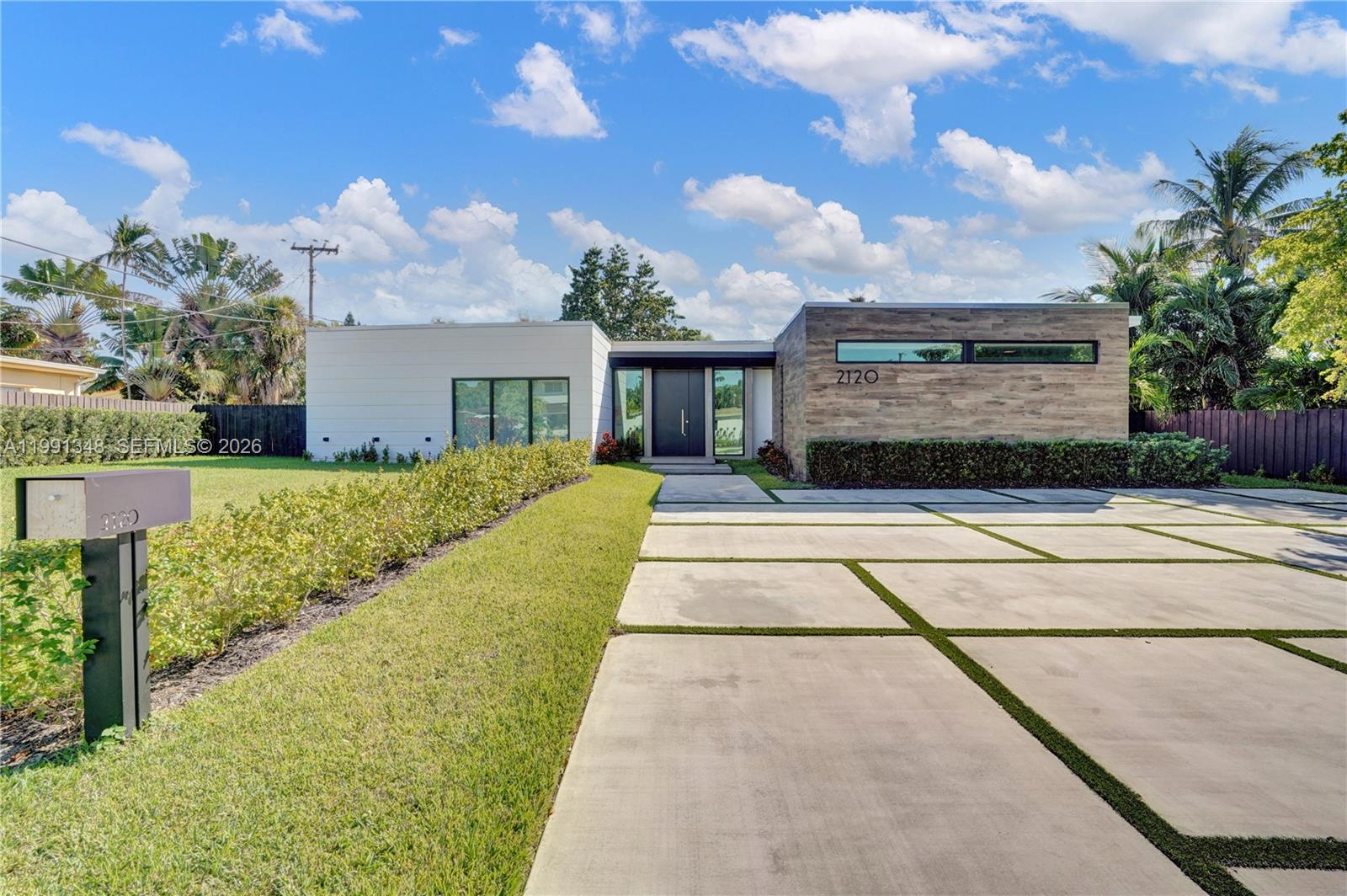 A modern single-story house features a wood-paneled facade, white siding, and a concrete paver driveway — 2120 NE 197th Ter, Miami FL 33179, MIAMI, FL