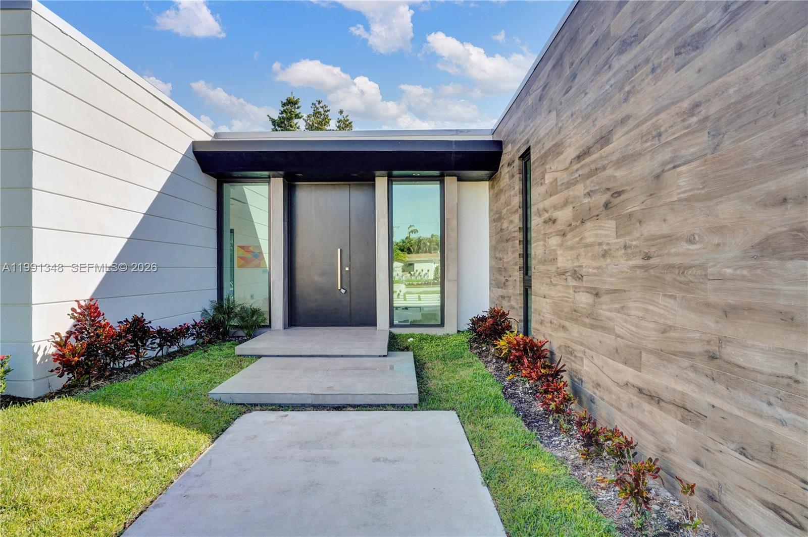 The exterior of a modern home features a dark double door, wood-look siding, and concrete steps — 2120 NE 197th Ter, Miami FL 33179, MIAMI, FL