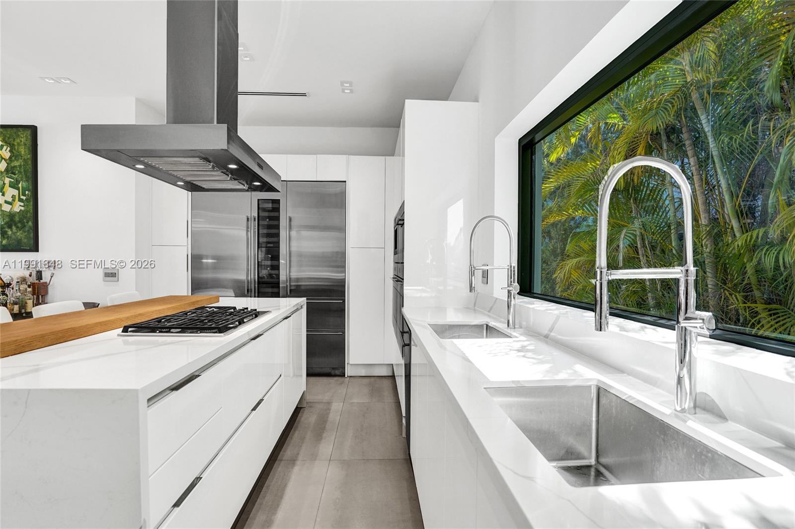 A modern white kitchen features a large island, stainless steel appliances, and a long window — 2120 NE 197th Ter, Miami FL 33179, MIAMI, FL