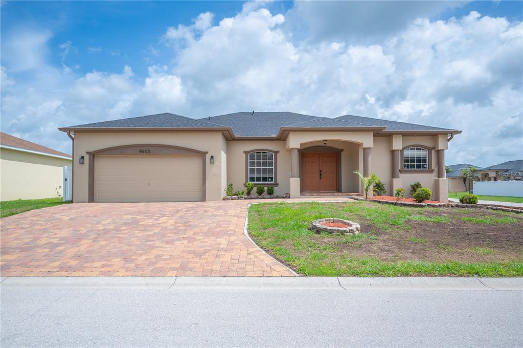 A single-story house with a tan stucco exterior, a paver driveway, and a two-car garage — 8653 PEBBLEBROOKE WAY, LAKELAND, FL