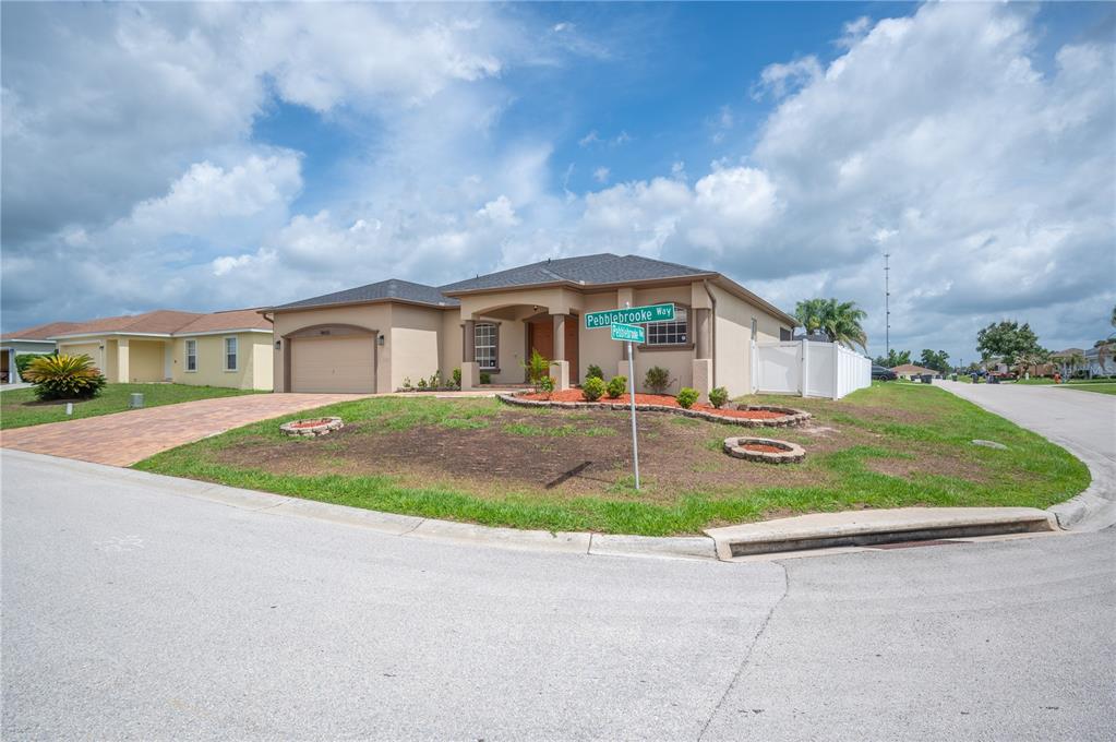 A single-story tan stucco house with a two-car garage sits on a corner lot — 8653 PEBBLEBROOKE WAY, LAKELAND, FL