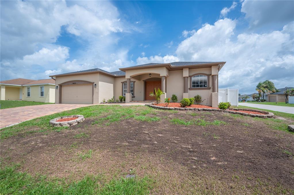 A beige single-story house with a two-car garage and a partially landscaped front yard — 8653 PEBBLEBROOKE WAY, LAKELAND, FL
