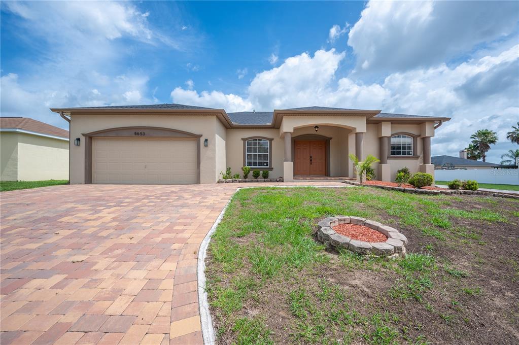 A single-story house with a tan stucco exterior, a paved driveway, and a front entryway — 8653 PEBBLEBROOKE WAY, LAKELAND, FL