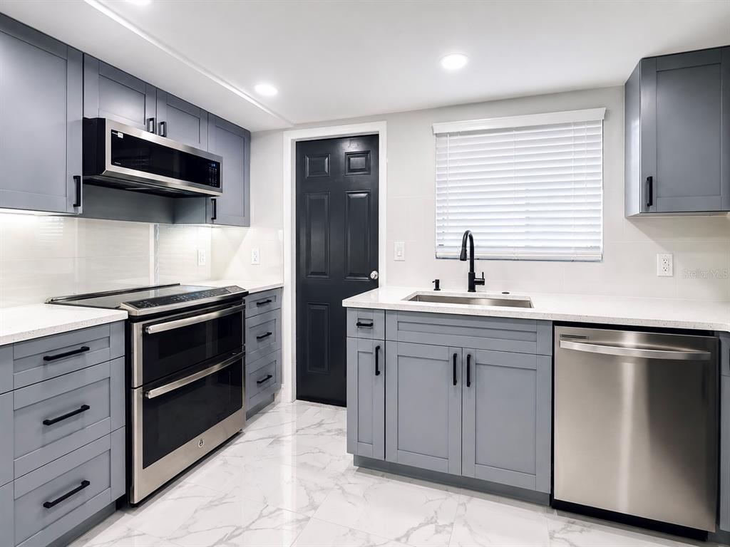 A modern kitchen features gray cabinets, stainless steel appliances, white countertops, and marble-patterned tile flooring — 12414 TOUCHTON DRIVE UNIT 98, TAMPA, FL