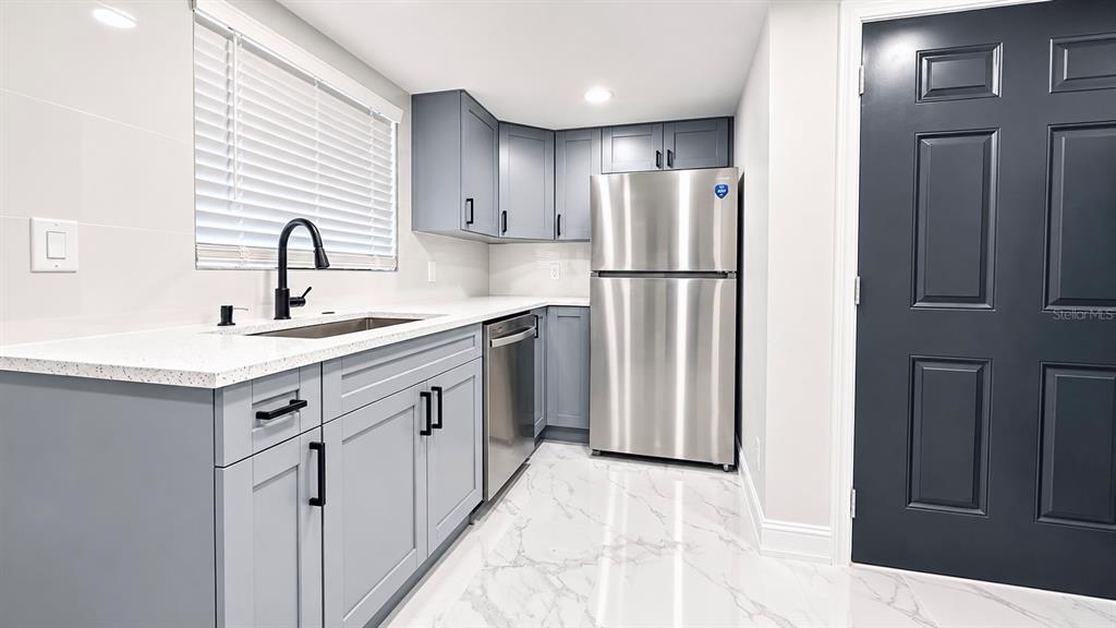 A modern kitchen features gray cabinets, stainless steel appliances, white countertops, and marble-look tile flooring — 12414 TOUCHTON DRIVE UNIT 98, TAMPA, FL