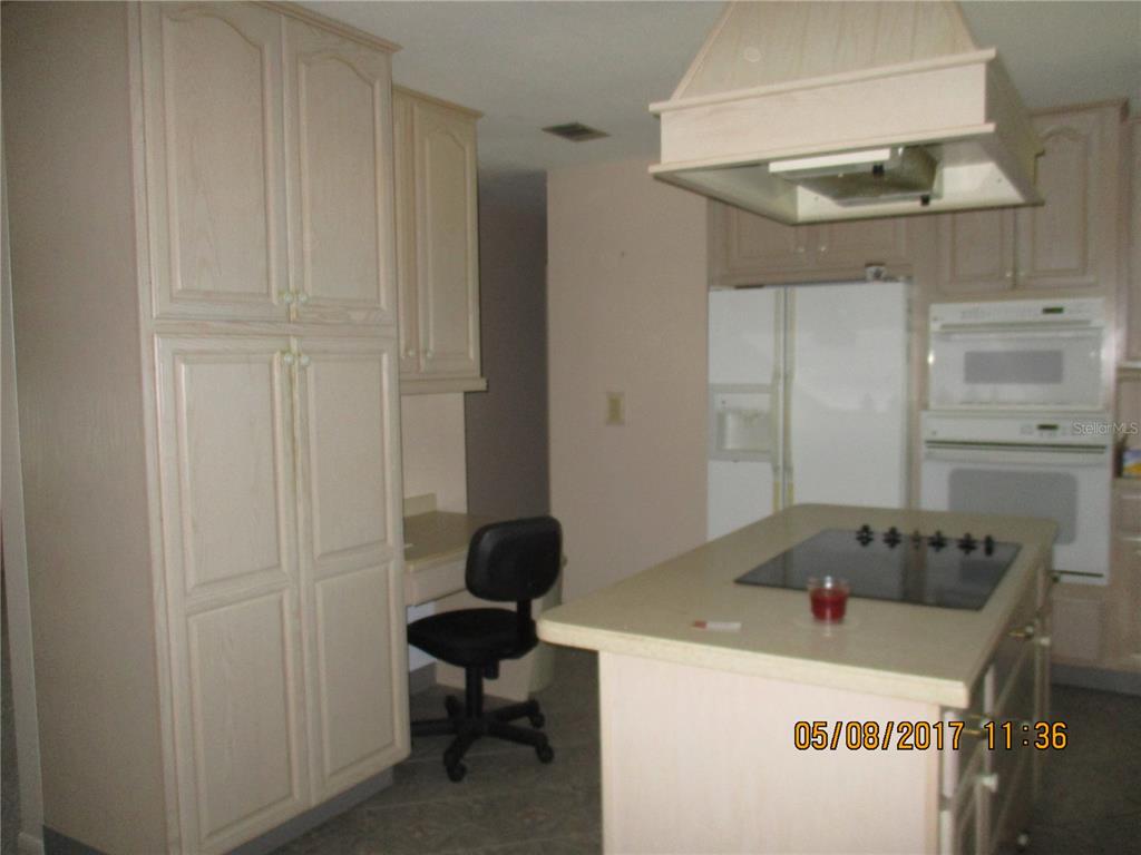 A kitchen features light-colored cabinetry, a central island with a cooktop, and a built-in desk — 8228 SAN JACINTO AVENUE, NORTH PORT, FL