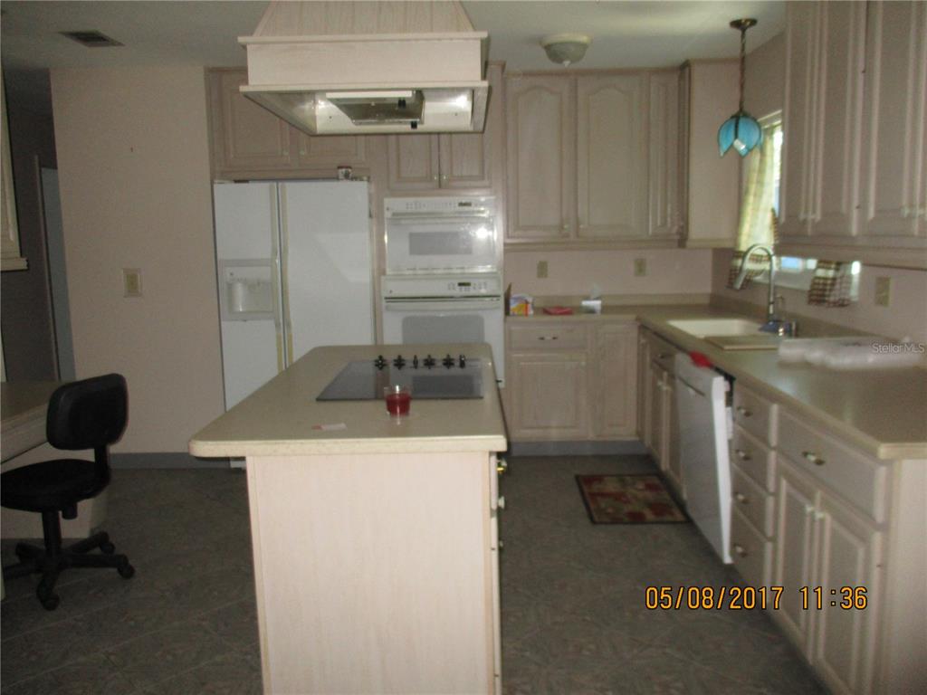 A kitchen features light-colored cabinets, a central island with a cooktop, and white appliances — 8228 SAN JACINTO AVENUE, NORTH PORT, FL