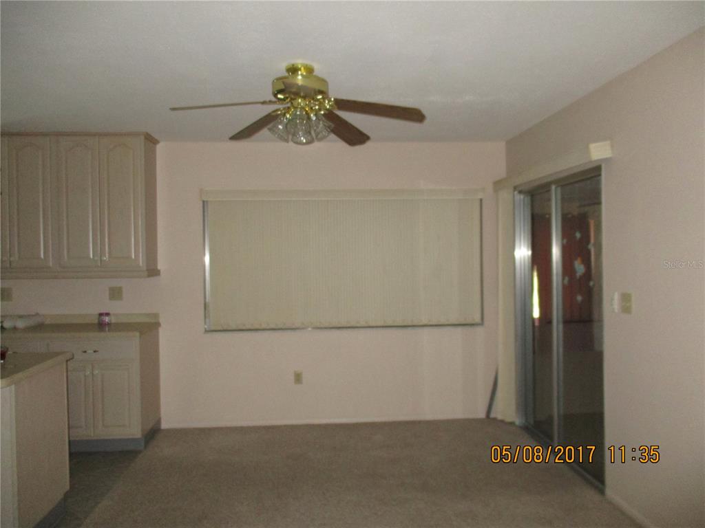 A dining area features a ceiling fan, beige carpet, light-colored cabinets, and a sliding glass door — 8228 SAN JACINTO AVENUE, NORTH PORT, FL