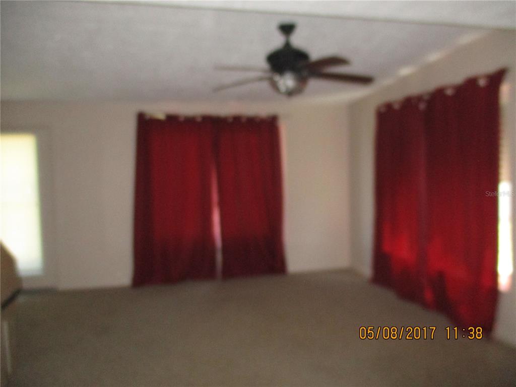 A carpeted living room features a ceiling fan and two windows covered by red curtains — 8228 SAN JACINTO AVENUE, NORTH PORT, FL