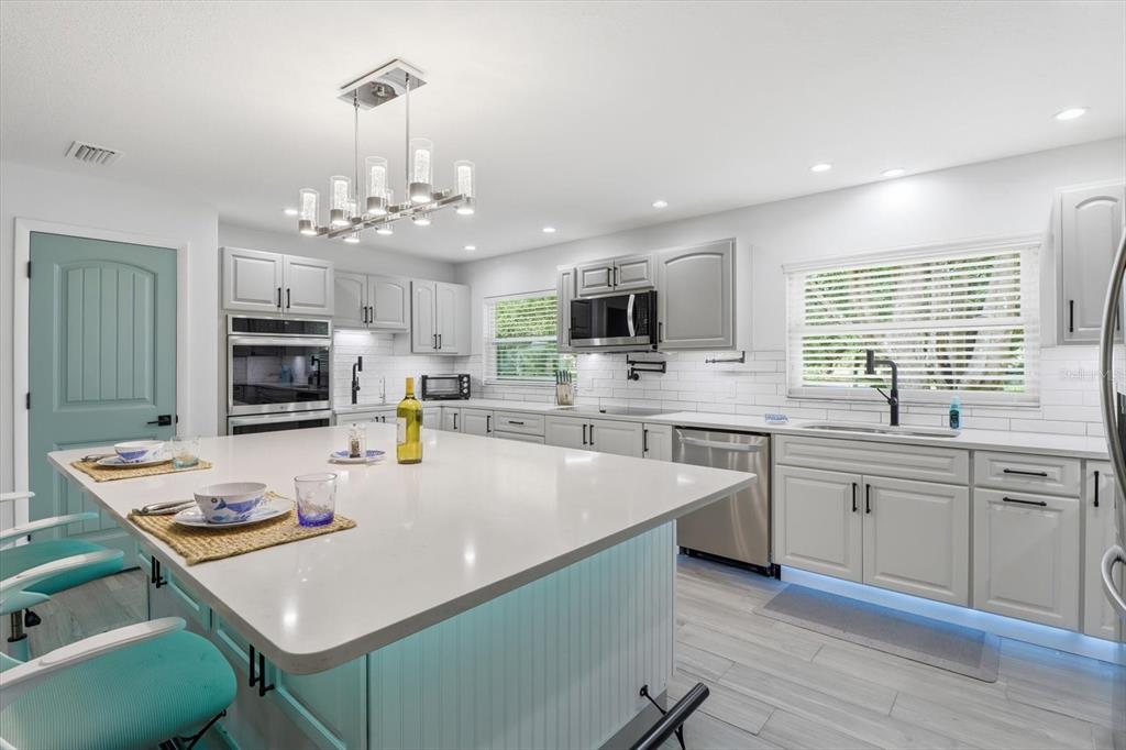A modern kitchen features a large white island, gray cabinetry, stainless steel appliances, and teal accents — 5109 S RUNNING BROOK DRIVE, HOMOSASSA, FL