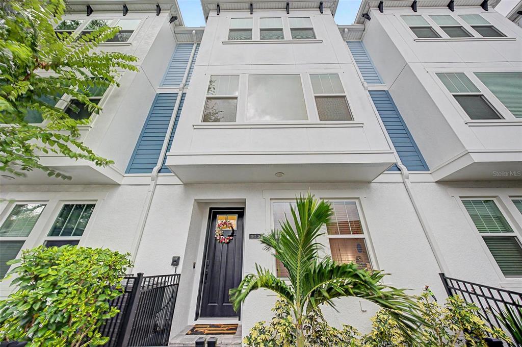 A low-angle exterior view of a three-story white townhouse with blue accents and palm trees — 6605 N NEBRASKA AVENUE UNIT 28, TAMPA, FL