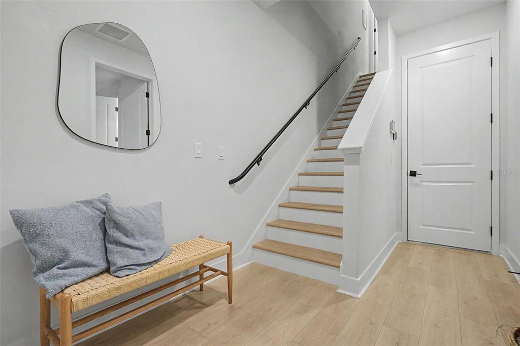 A modern entryway features a wooden bench, a wall mirror, and stairs with a black railing — 6605 N NEBRASKA AVENUE UNIT 28, TAMPA, FL