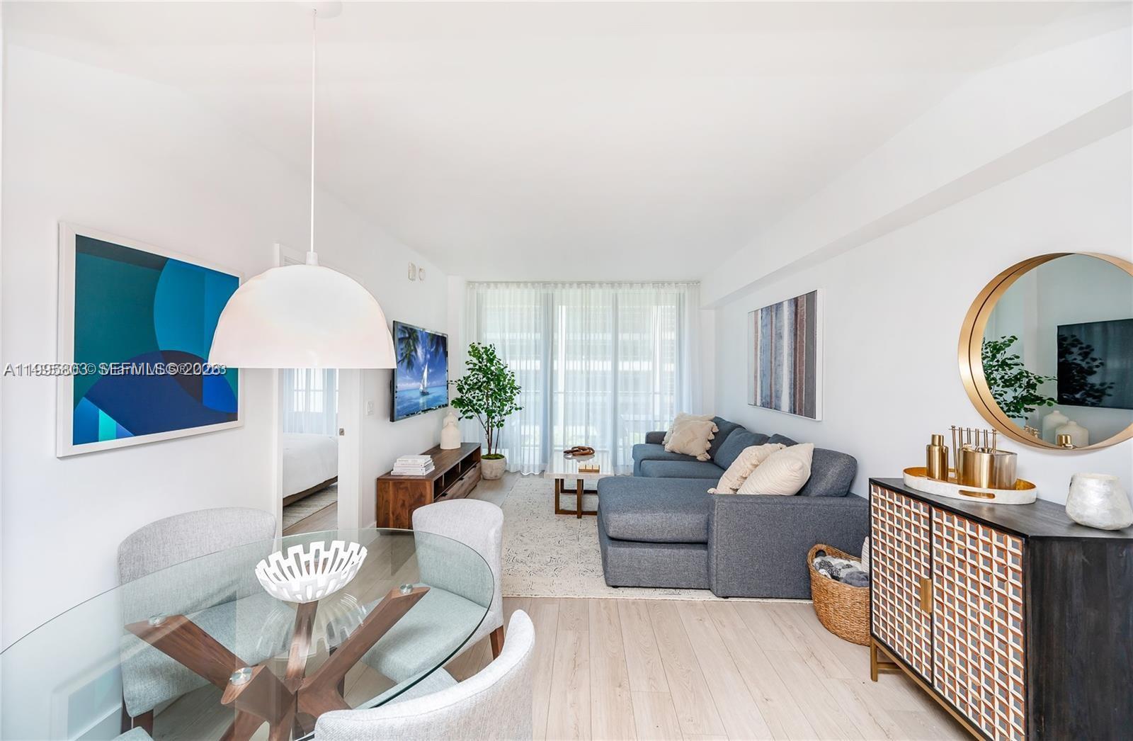 A living and dining area features a glass table, gray sectional sofa, and circular mirror — 121 NE 34th St # L402, Miami FL 33137, MIAMI, FL