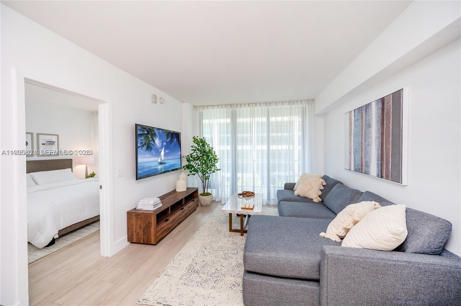 A living room features a grey sectional sofa, a wooden media console, and a television — 121 NE 34th St # L402, Miami FL 33137, MIAMI, FL