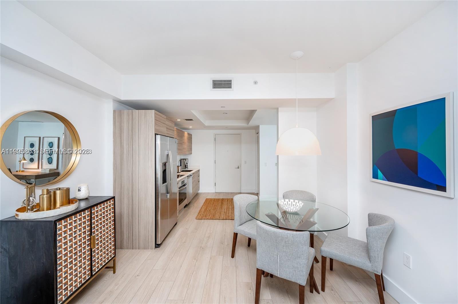 A modern kitchen and dining area features light wood flooring, a glass table, and cabinetry — 121 NE 34th St # L402, Miami FL 33137, MIAMI, FL