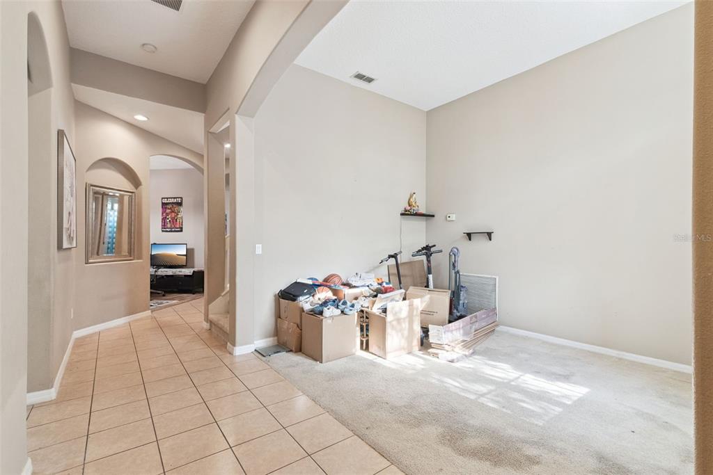A tiled hallway leads to a carpeted room containing several cardboard boxes and two scooters — 16249 TUDOR GROVE DRIVE, ORLANDO, FL