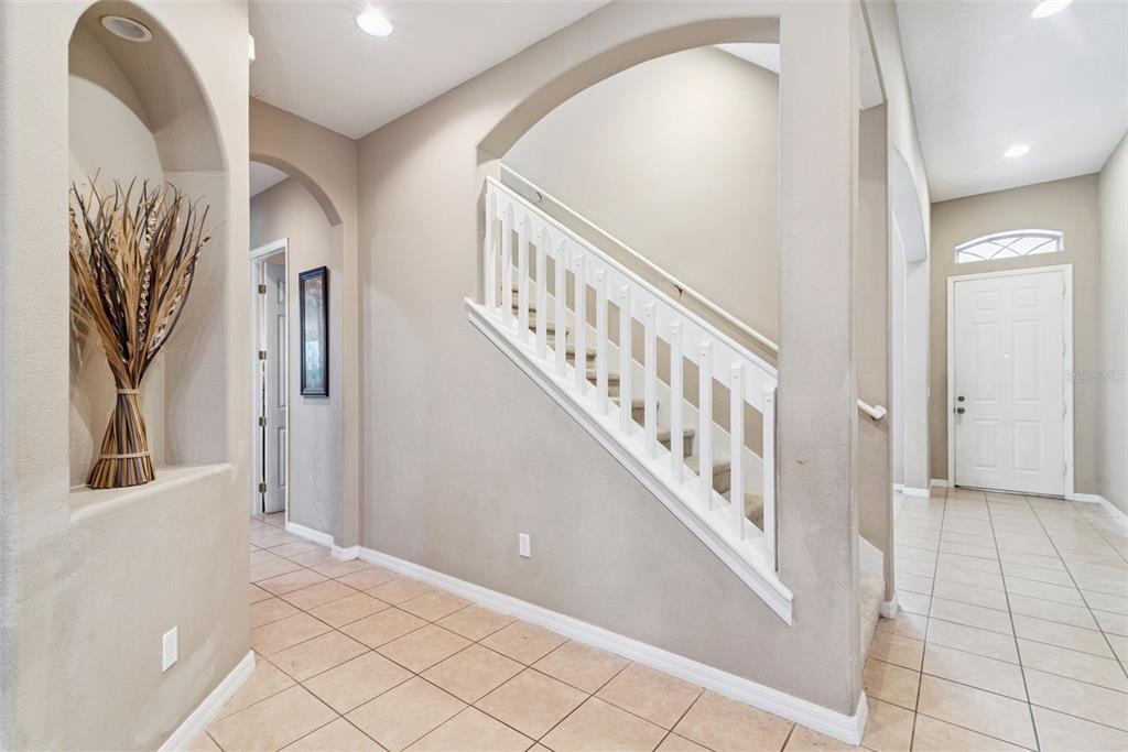 An interior entryway features a tiled floor, a staircase with white railings, and an arched niche — 16249 TUDOR GROVE DRIVE, ORLANDO, FL
